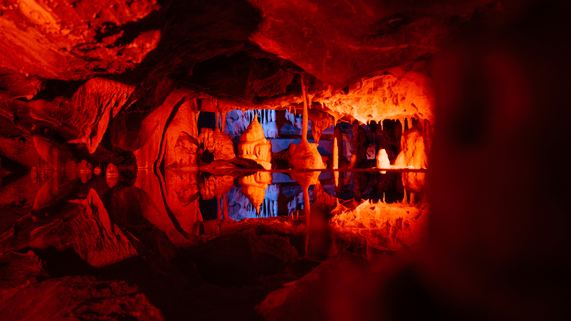 The inside of a cave lit up in red with a pool of water reflecting the rock formations