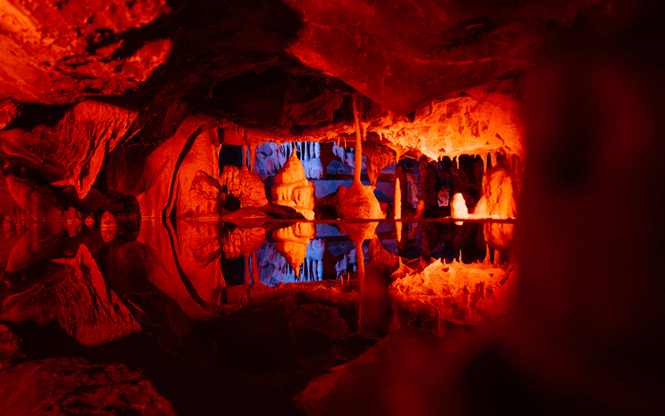 The inside of a cave lit up in red with a pool of water reflecting the rock formations