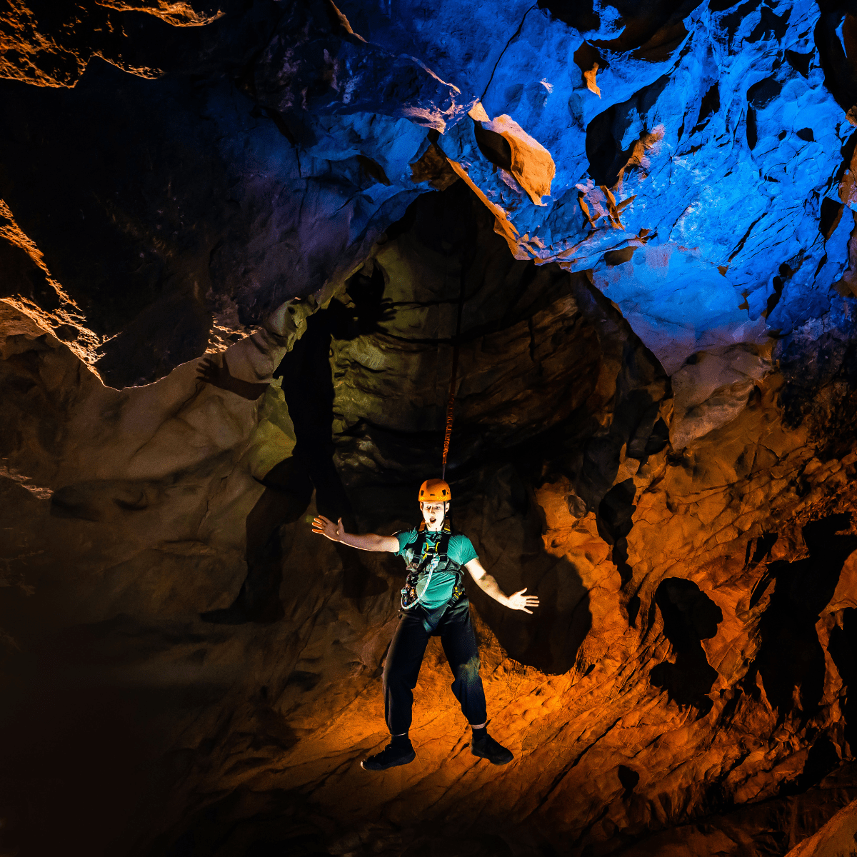 A visitor hangs in the cave after completing the Black Cat Freefall. The caves behind him are lit up in bold colours