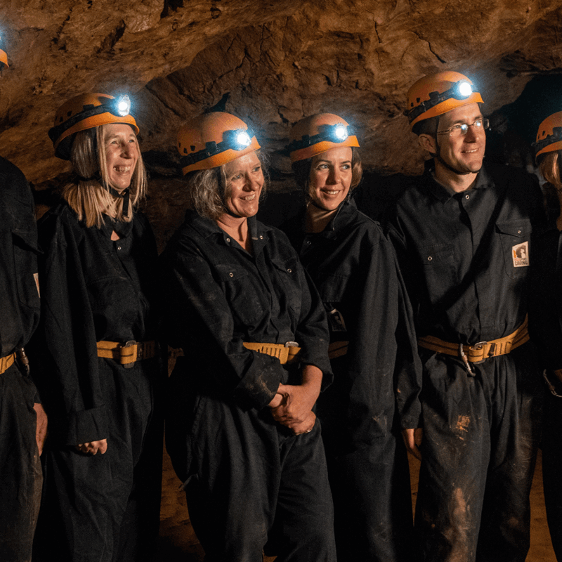 A group pose for a photograph in their overalls and head torches before they begin their adventure caving challenge