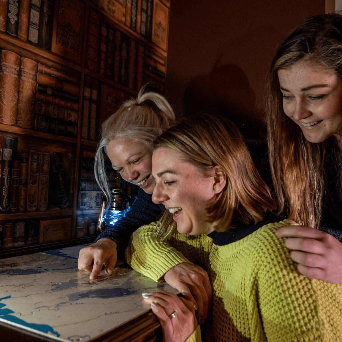A group of three look at a potential clue in the vault escape room at Cheddar gorge. They gather round a map looking for answers