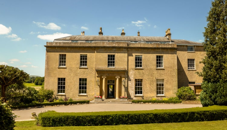 The Bishopstrow Hotel - A large, brown building with pillars at the entrance and trees and lawn outside