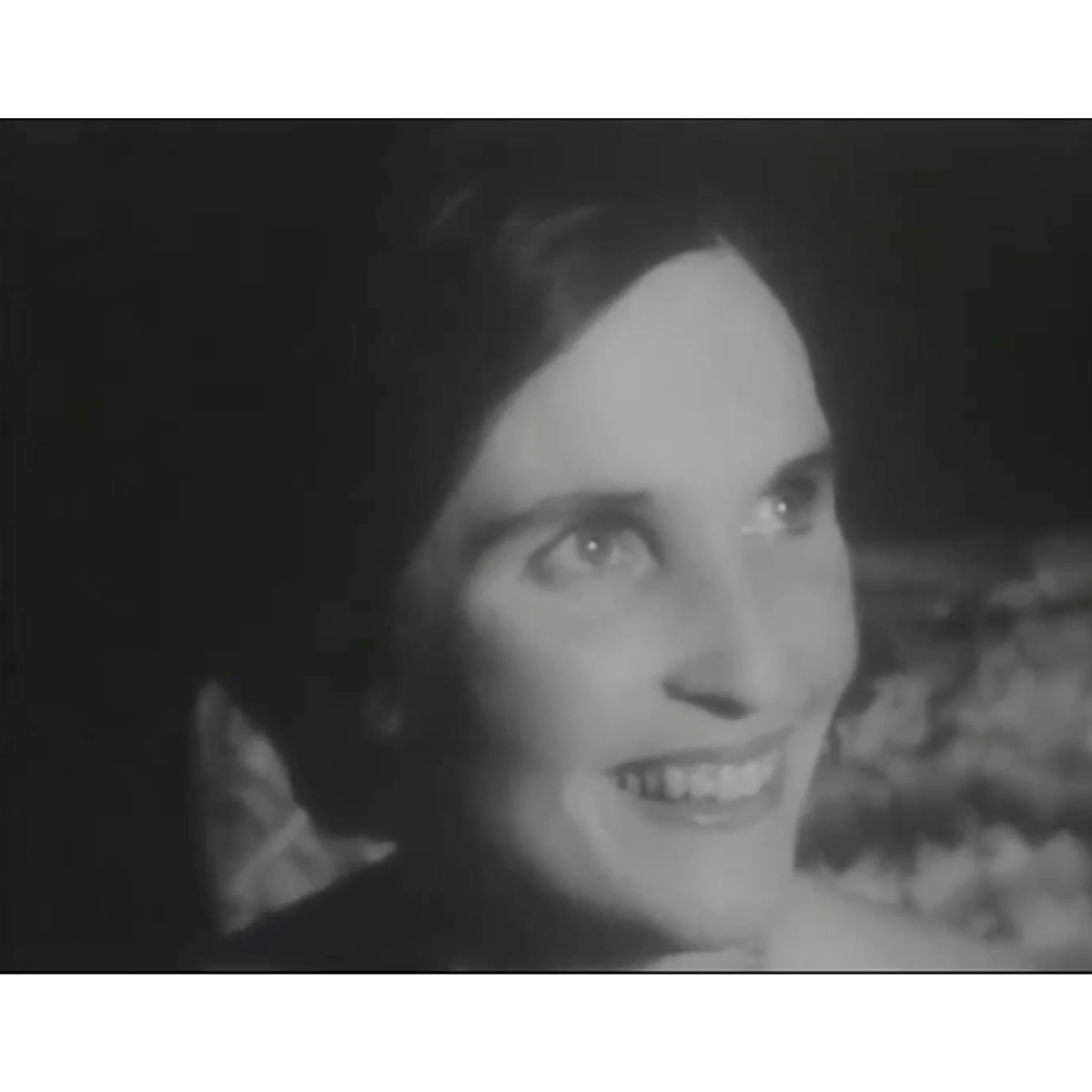 Black and white photo of a lady with her hair tied back, smiling to the side of the camera