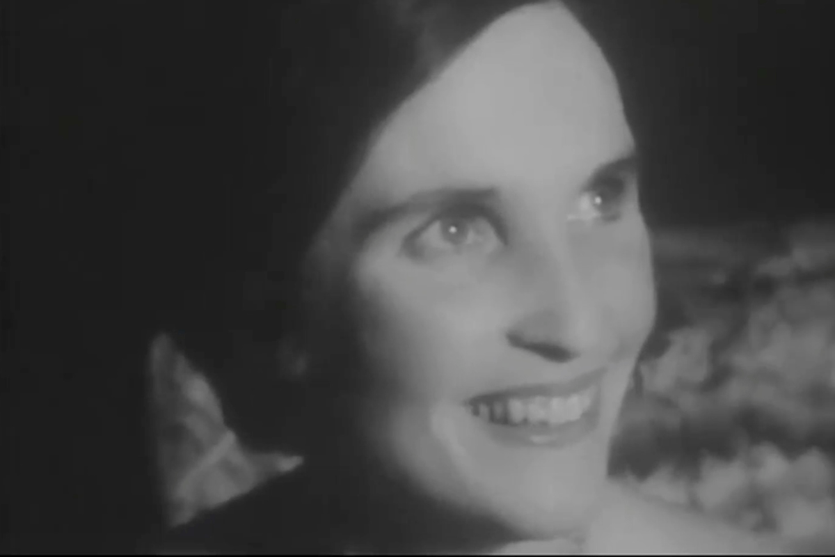 Black and white photo of a lady with her hair tied back, smiling to the side of the camera