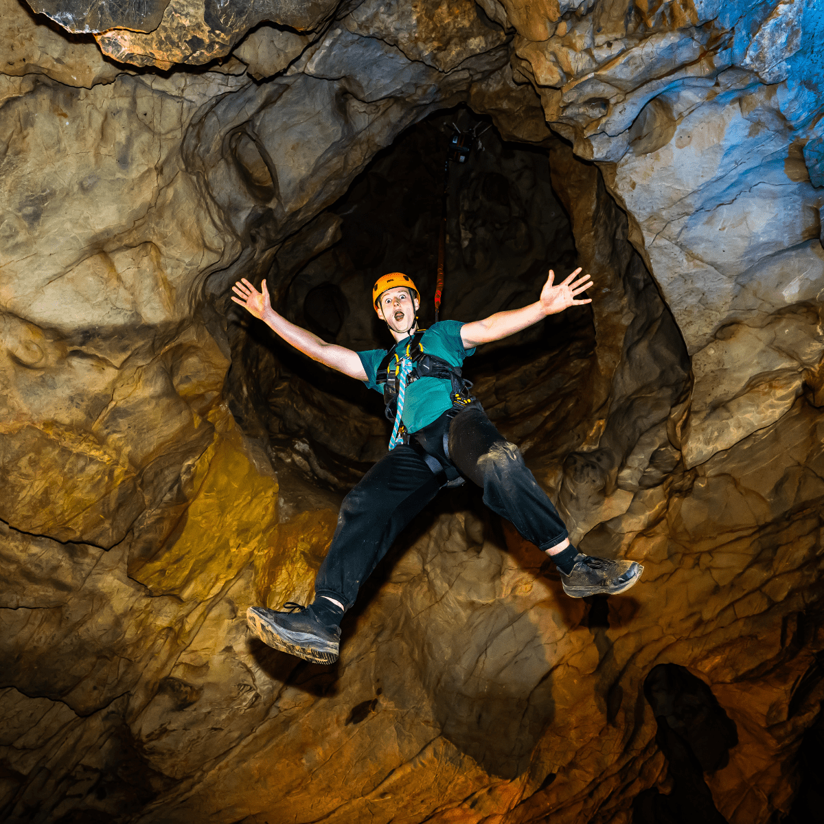 A visitor at Cheddar Gorge, enjoying the Black Cat Freefall activity, as they hang in the cave with limbs outstretched and a huge grin