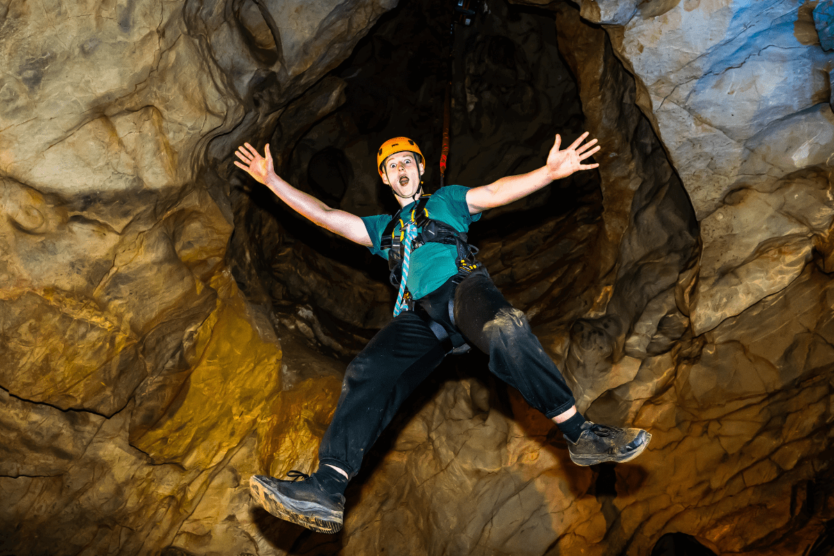 A visitor at Cheddar Gorge, enjoying the Black Cat Freefall activity, as they hang in the cave with limbs outstretched and a huge grin