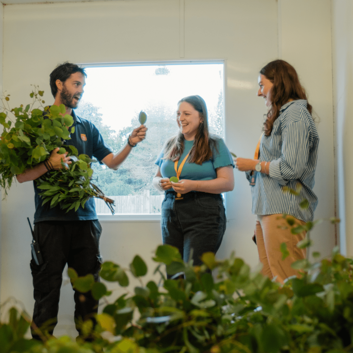 Two VIP guests laugh as an animal team member holds a large bunch of eucalyptus and talks to them