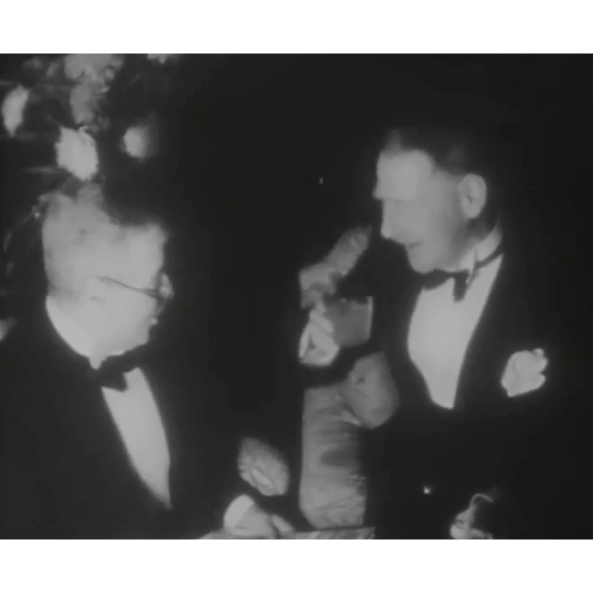 Black and white image of two men in suits engaging in conversation