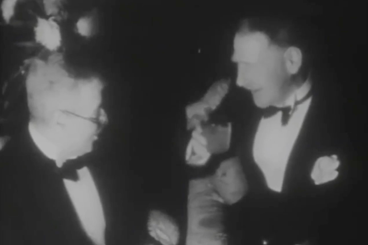 Black and white image of two men in suits engaging in conversation