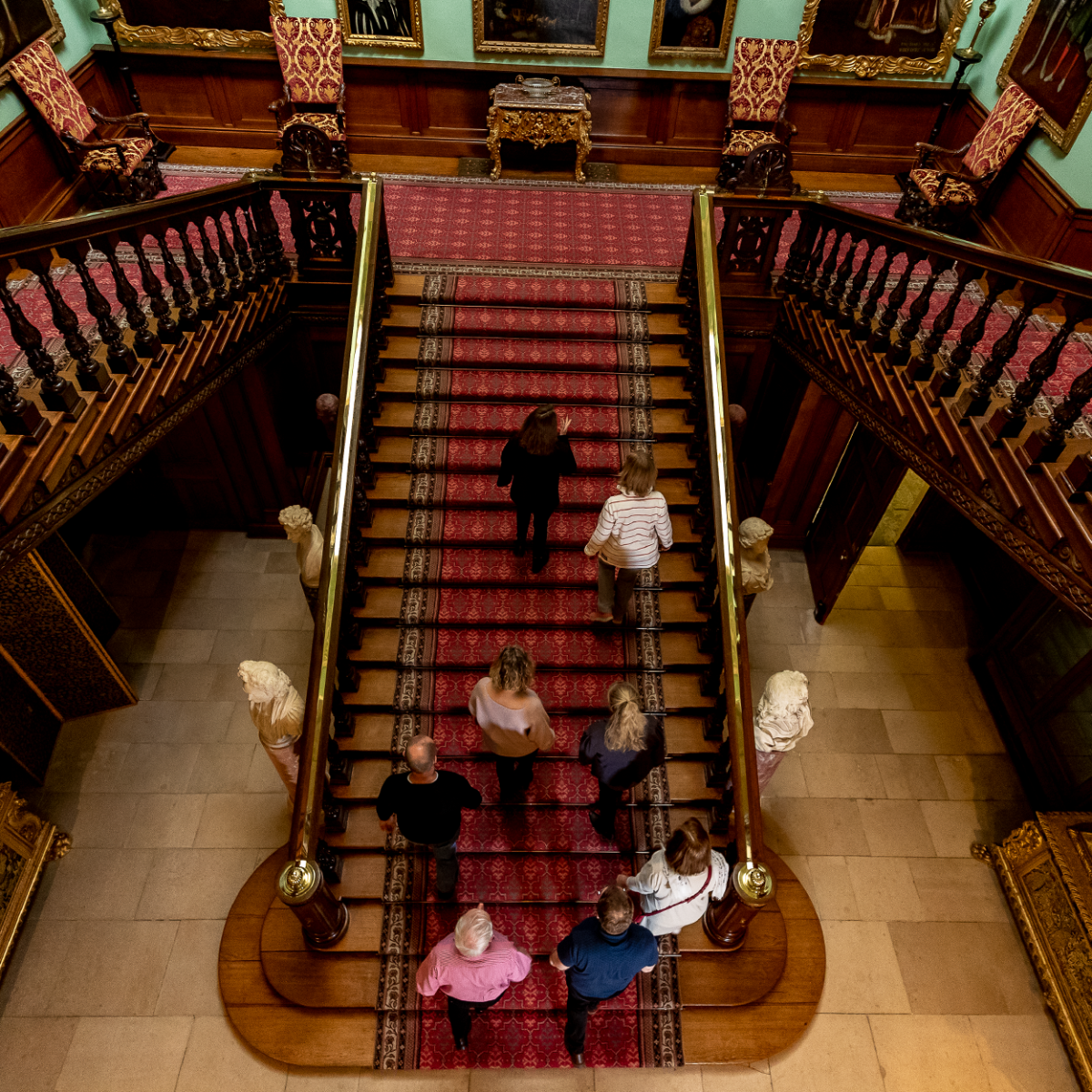 A group of people are seen from above, walking up the exquisite Grand Staircase of Longleat House from the ground floor