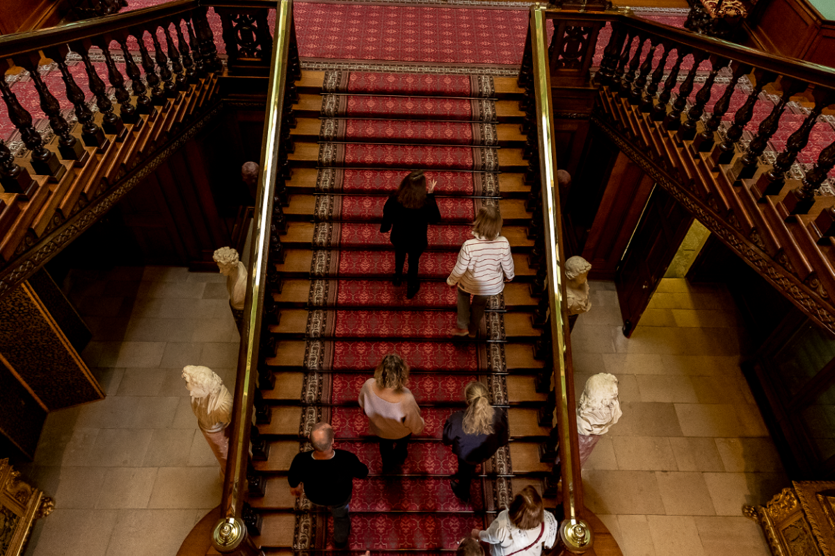 A group of people are seen from above, walking up the exquisite Grand Staircase of Longleat House from the ground floor