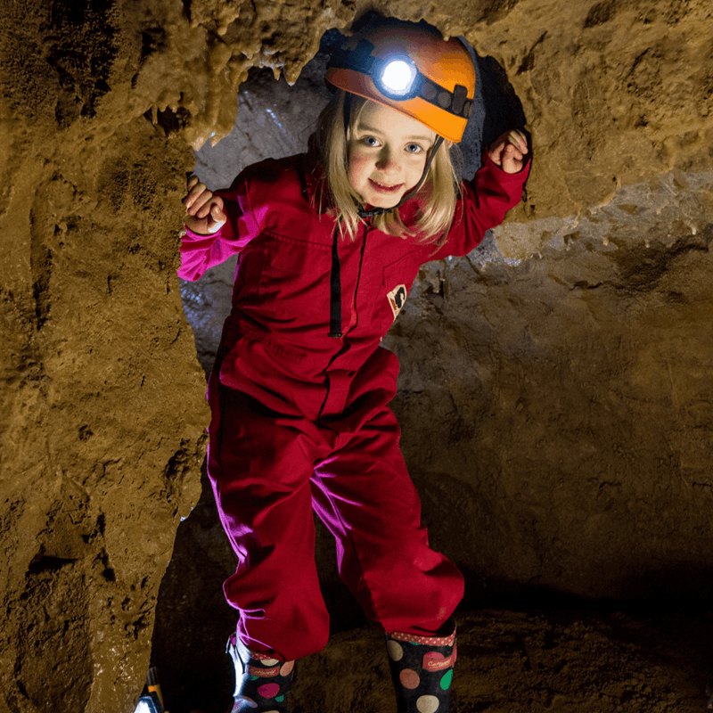 A young girl enjoys taking part in adventure caving, showing her head torch and overalls as she enters through a rock gap