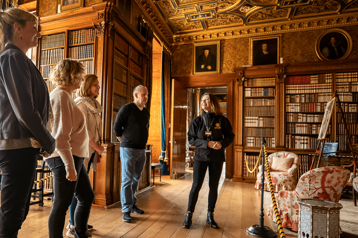 A Longleat House Guide delivers a tour to a group of people within one of the grand libraries