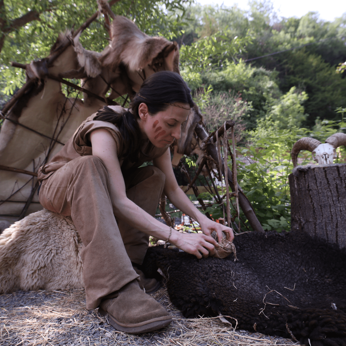 An instructor performs a demonstration for a Stone Age education session, dressed in natural-coloured clothing and brown stripes painted on her face
