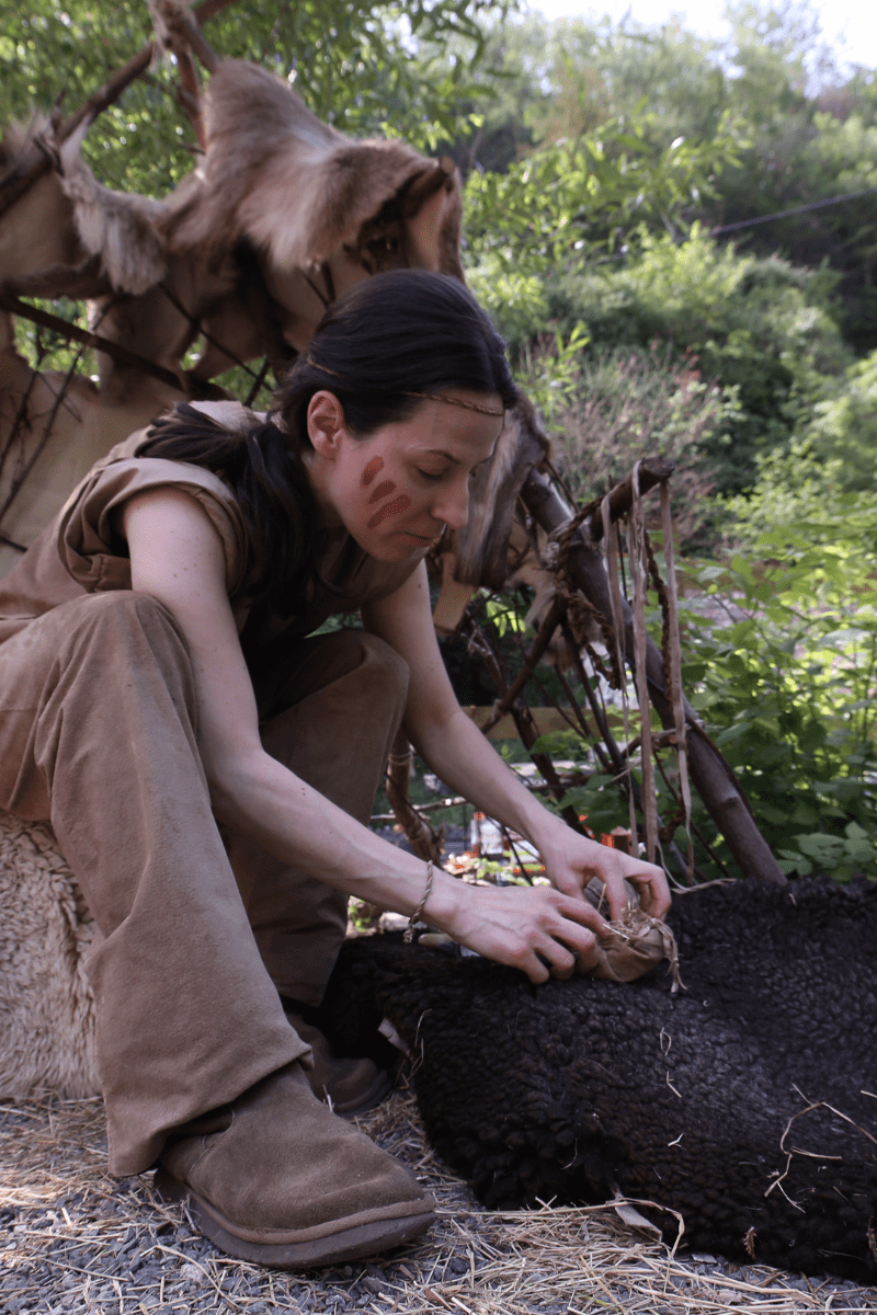 An instructor performs a demonstration for a Stone Age education session, dressed in natural-coloured clothing and brown stripes painted on her face