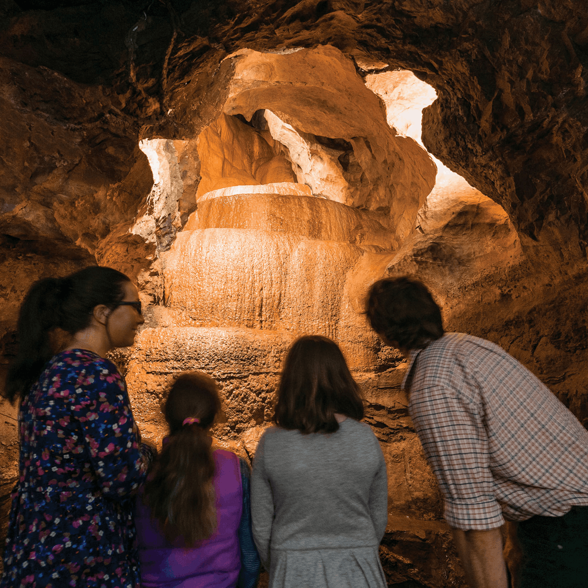 A family (from behind) looking at a rock formation within a cave 