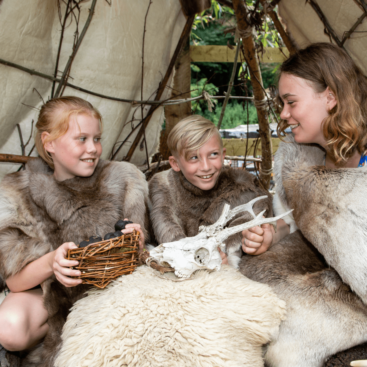 Three children, dressed in sheepskins and furs looking at a mock skull of an animal 