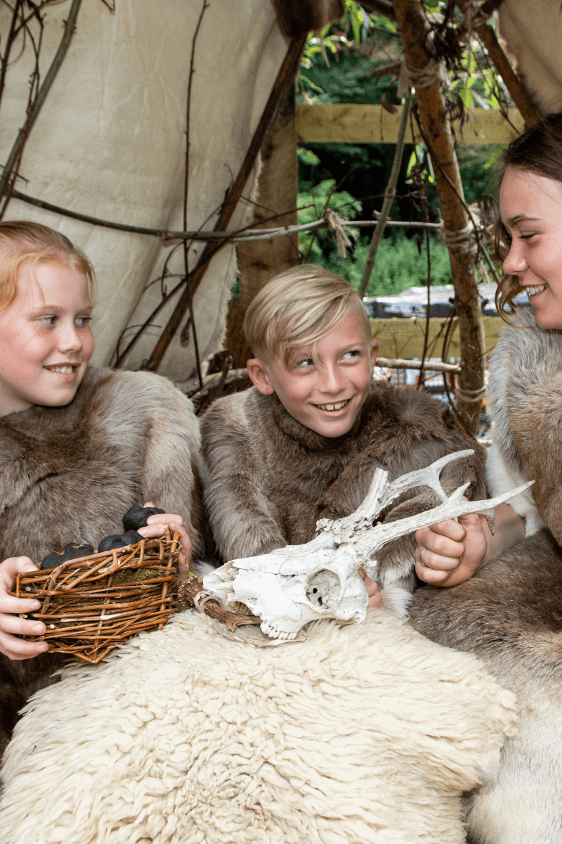 Three children, dressed in sheepskins and furs looking at a mock skull of an animal