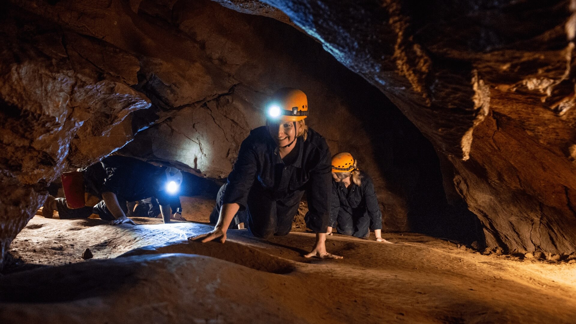 A group of people enjoying adventure caving at Cheddar Gorge as they crawl on their hands and knees with head torches lighting their way