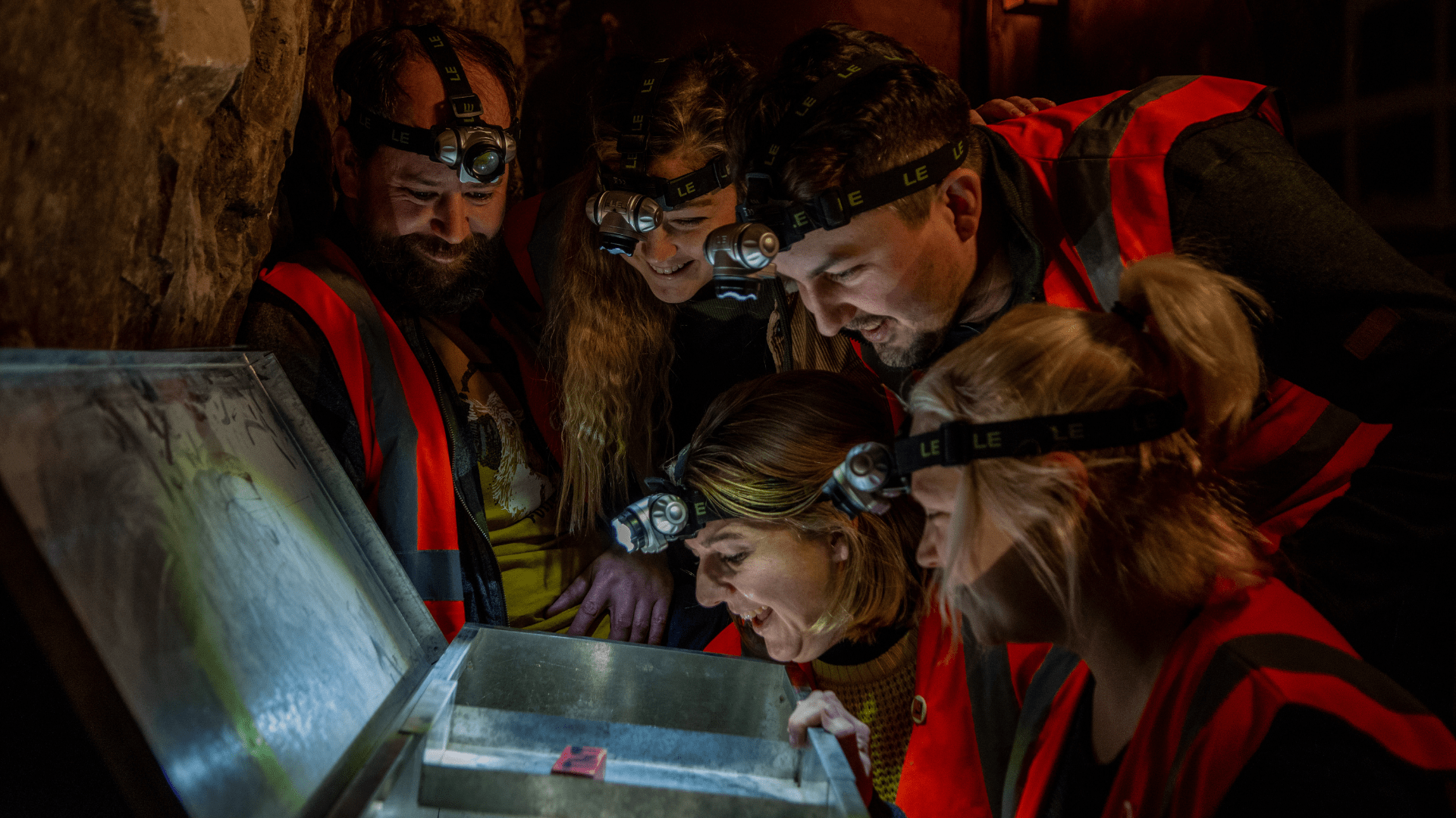 A group of visitors look into a lit up chest, looking for clues in one of the escape rooms