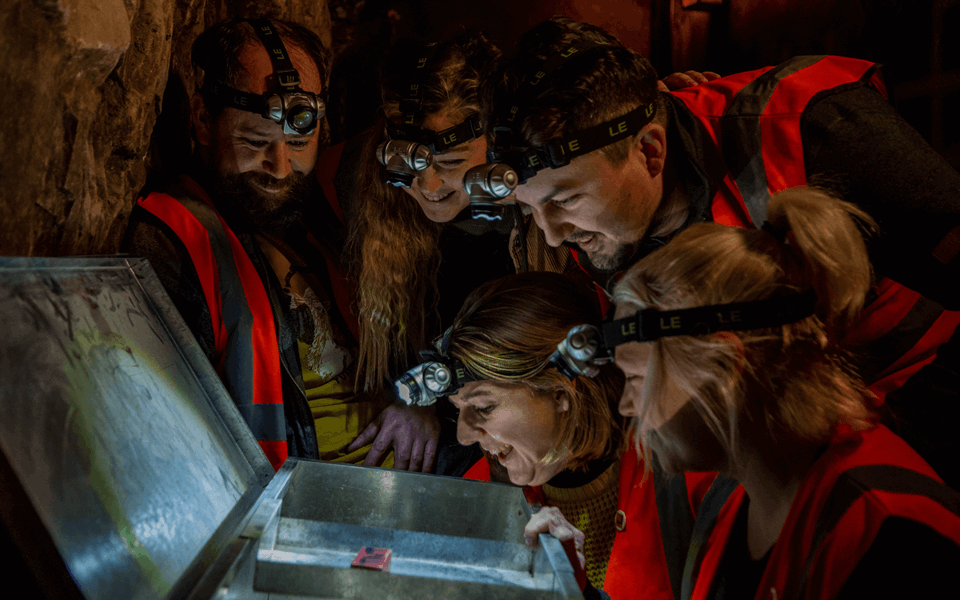 A group of visitors look into a lit up chest, looking for clues in one of the escape rooms