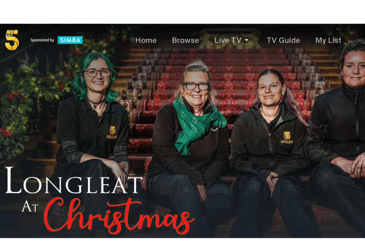 A promotional banner for Longleat at Christmas on Channel 5. Four staff members are sat on the bottom of the House staircase.