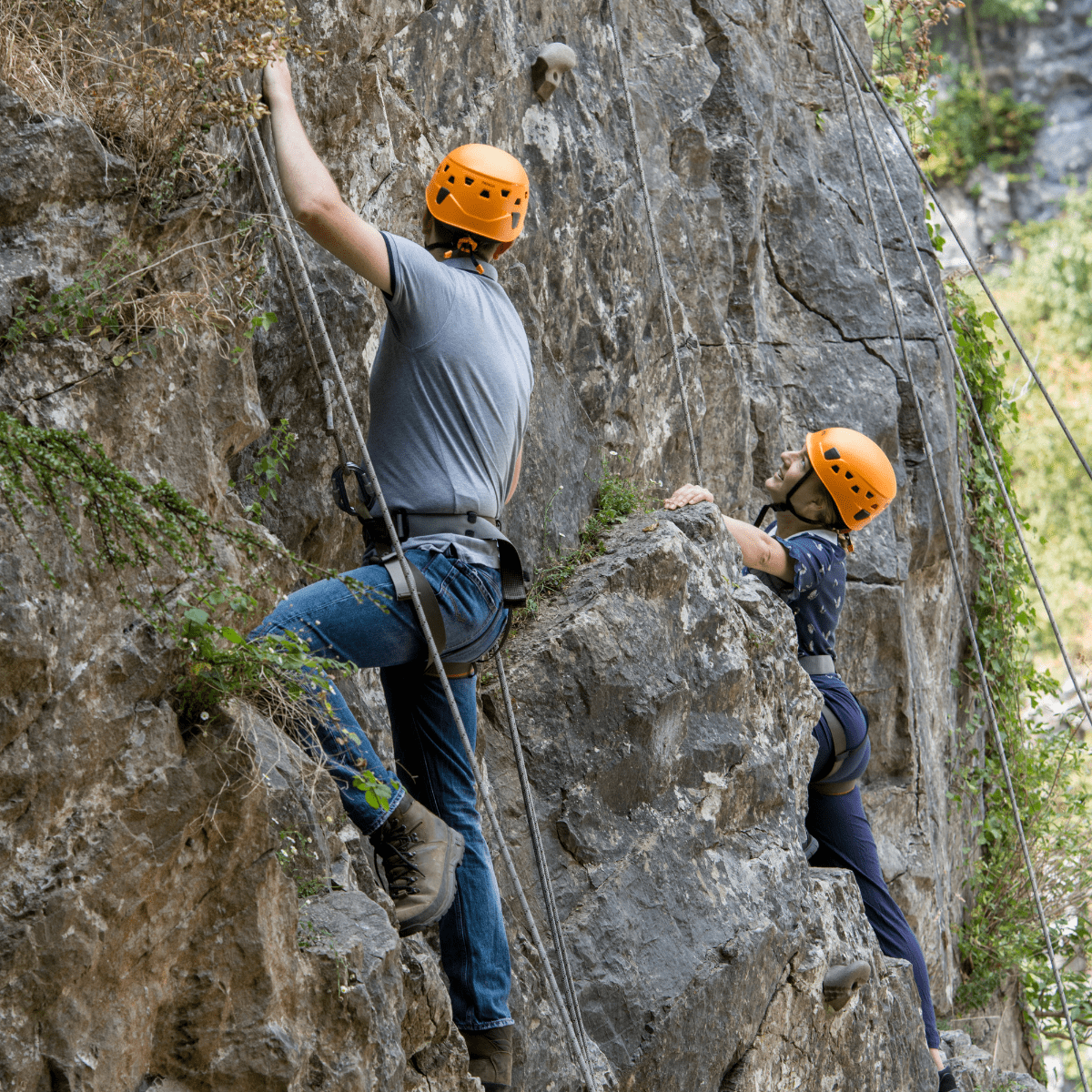 Two people climb the rock formations at Cheddar with safety lines and bright helmets