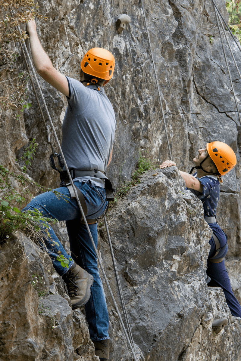Two people climb the rock formations at Cheddar with safety lines and bright helmets