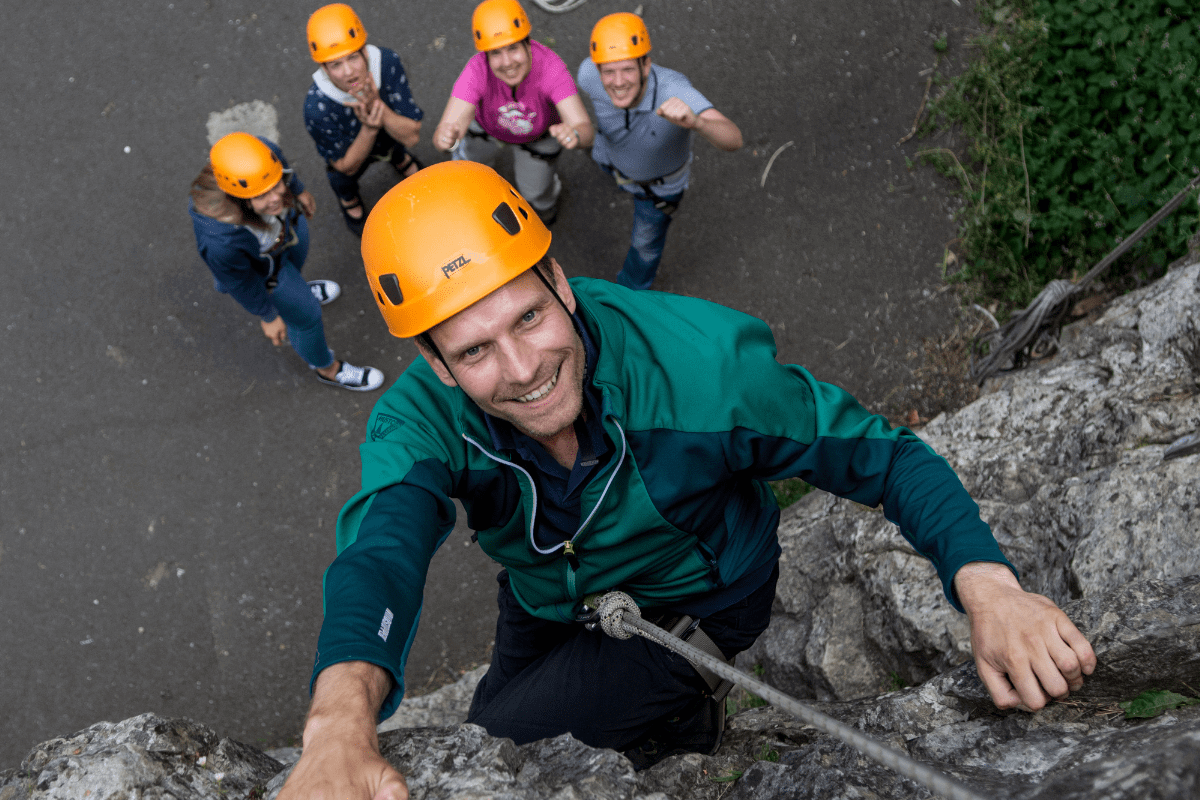 A visitor to Cheddar Gorge & Caves climbs one of the rock formations, with their team looking on in support and cheering