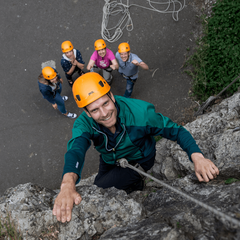 A visitor to Cheddar Gorge & Caves climbs one of the rock formations, with their team looking on in support and cheering