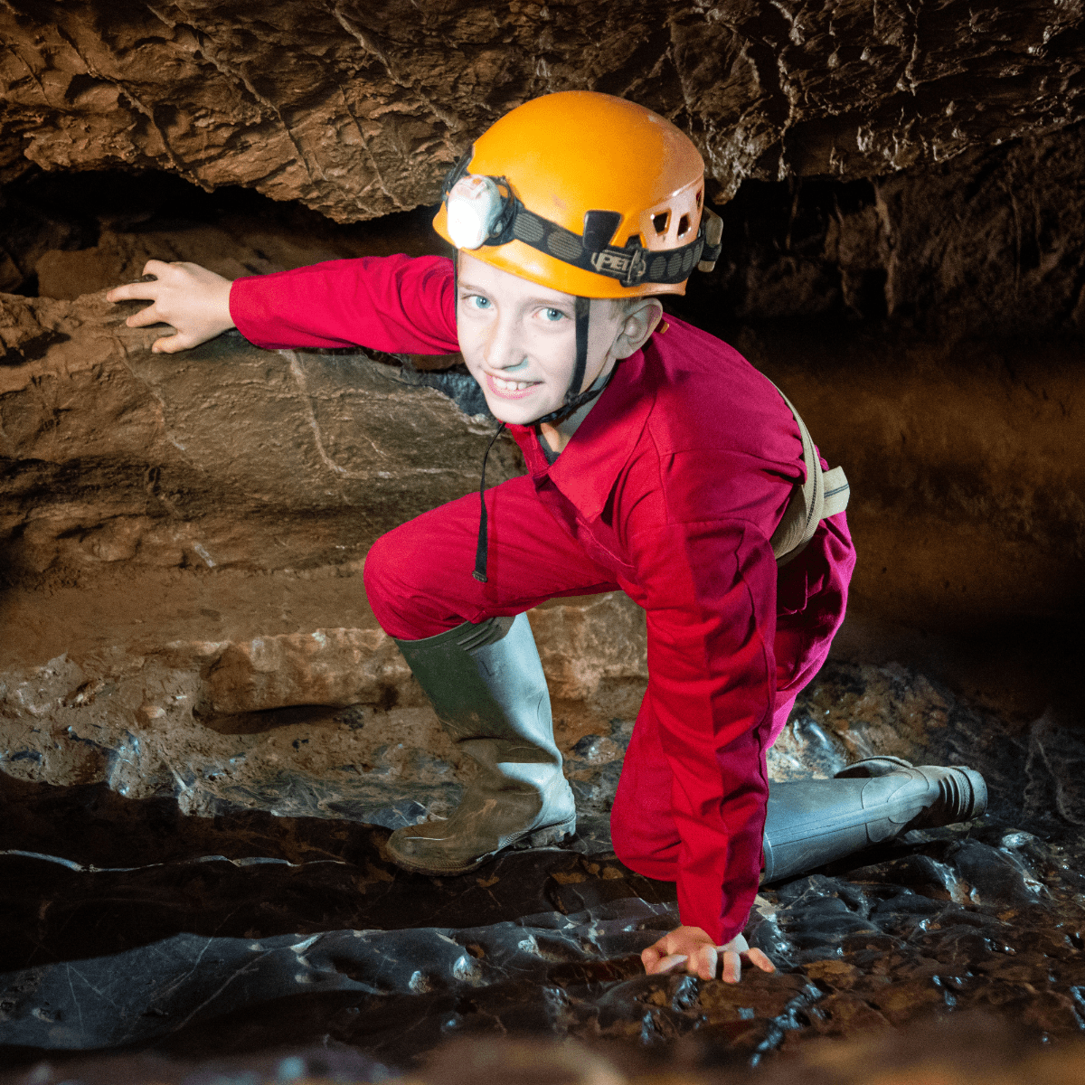 A young Adventure Caver navigates the cave floor, wearing overalls, wellies and head torch.