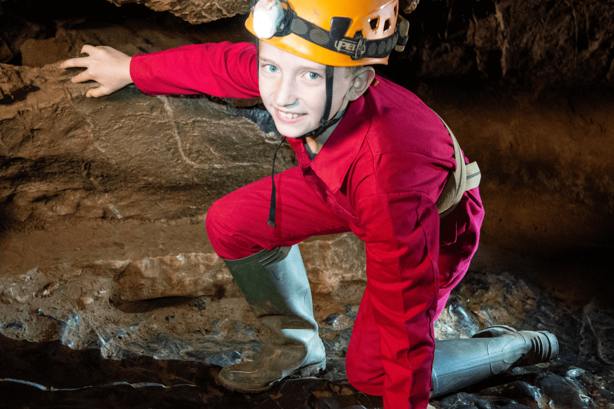 A young Adventure Caver navigates the cave floor, wearing overalls, wellies and head torch.
