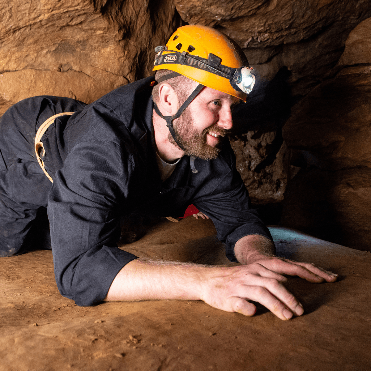 A visitor takes part in the Adventure Caving, as they crawl through one of the cave openings, with headtorch lighting the way