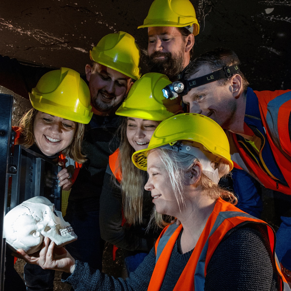 A group of people look at a potential clue in the escape rooms at Cheddar. They gather round scull looking for answers