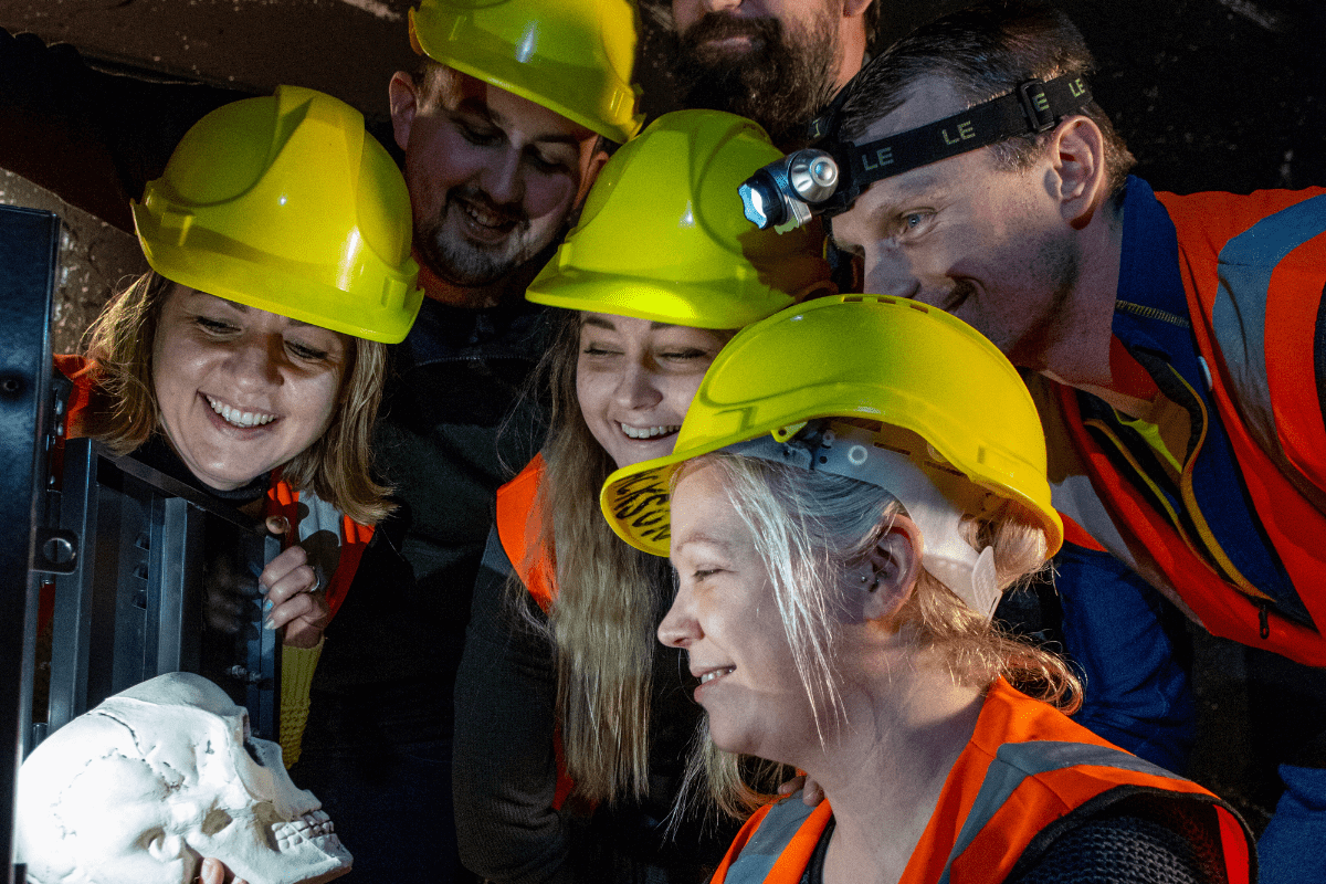 A group of people look at a potential clue in the escape rooms at Cheddar. They gather round scull looking for answers