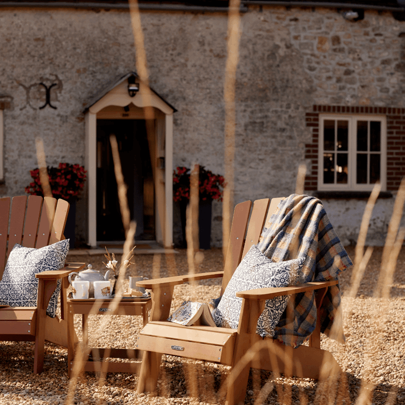 Two wooden seats with cushions and blankets in front of a farmhouse building