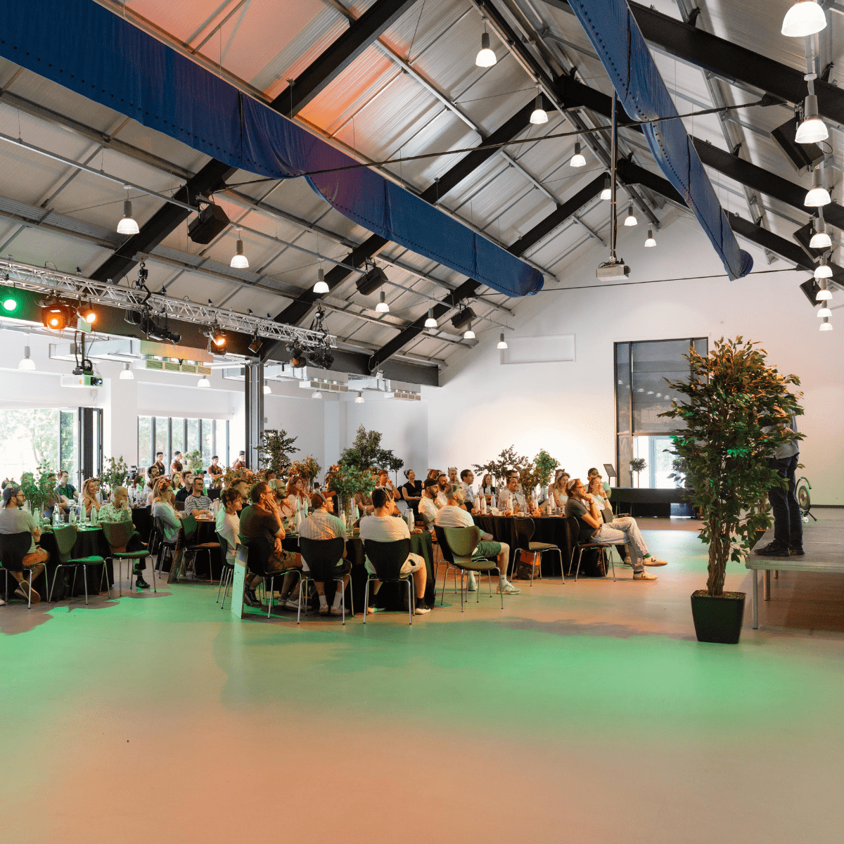 A large open plan room with a stage to the right and tables set cabaret style for the audience.
