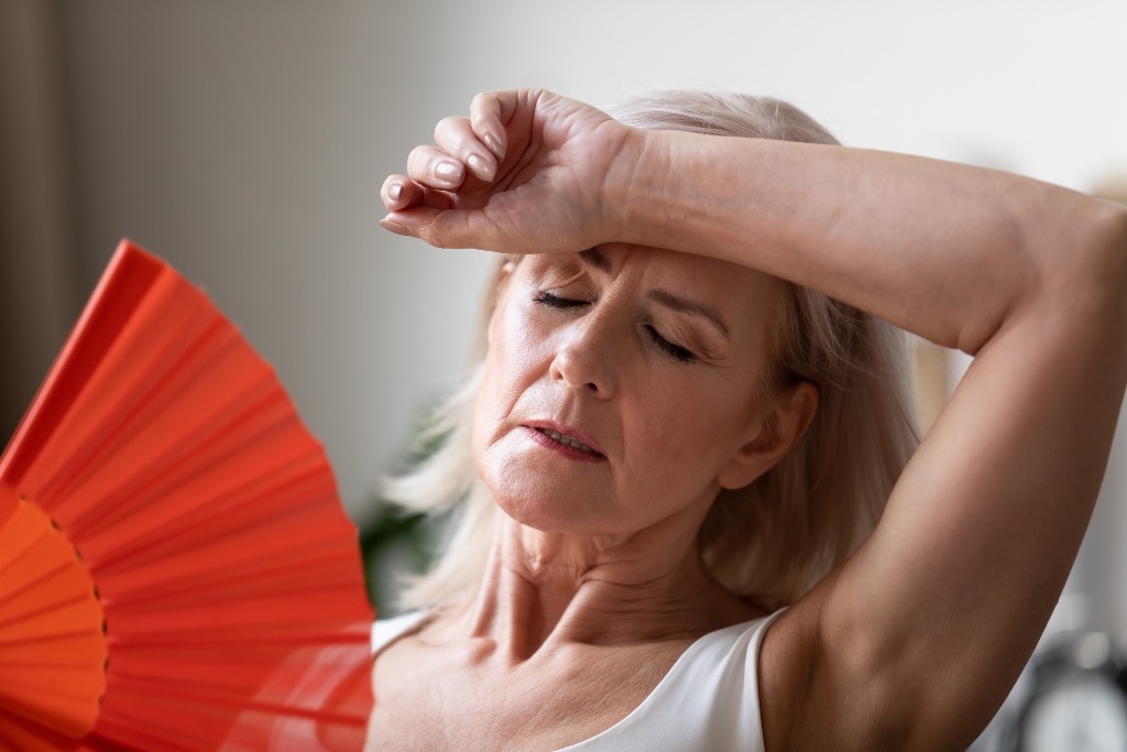 Woman in white top fanning herself with red folding fan