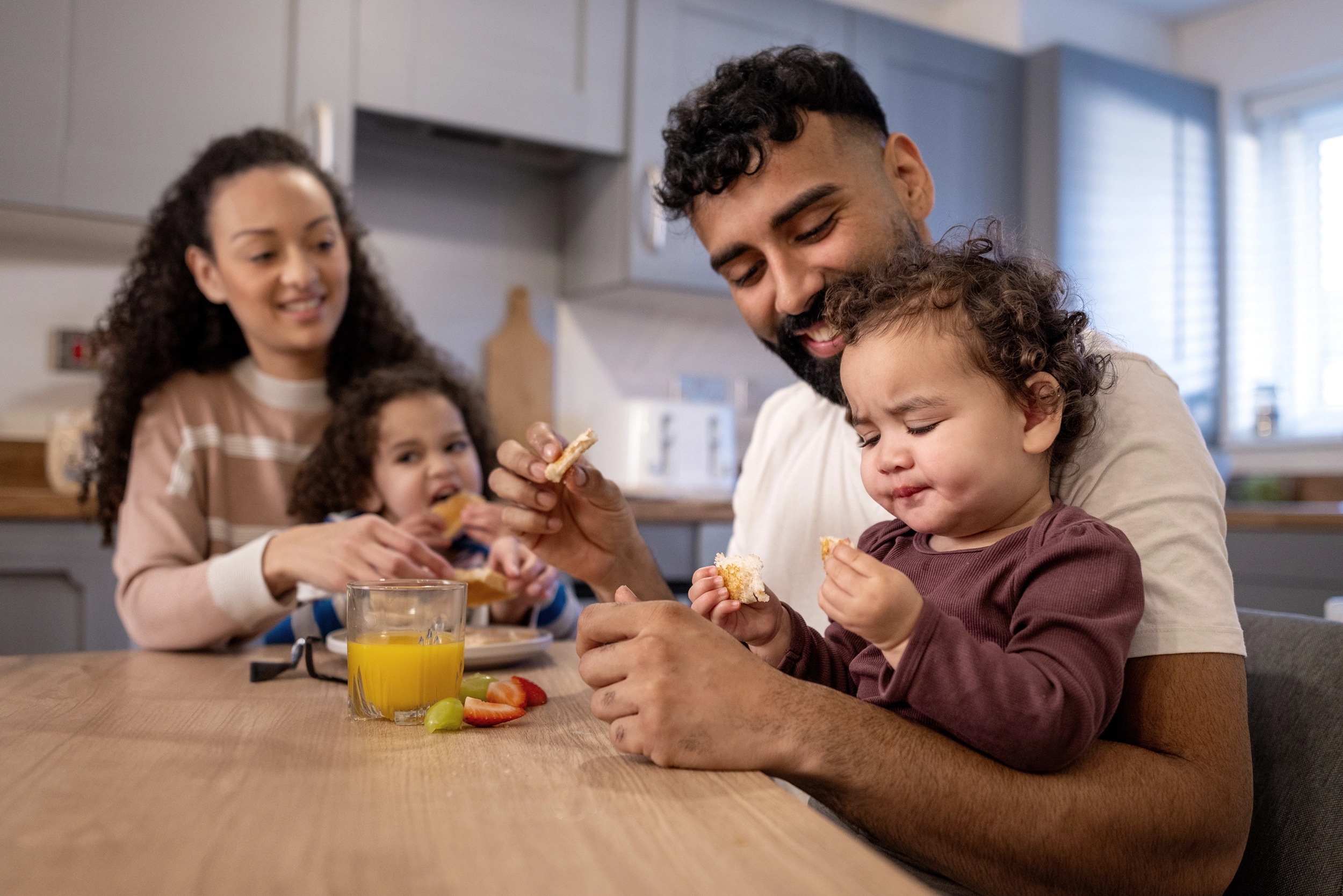 A mother and father with their two children eating food at the dinner table