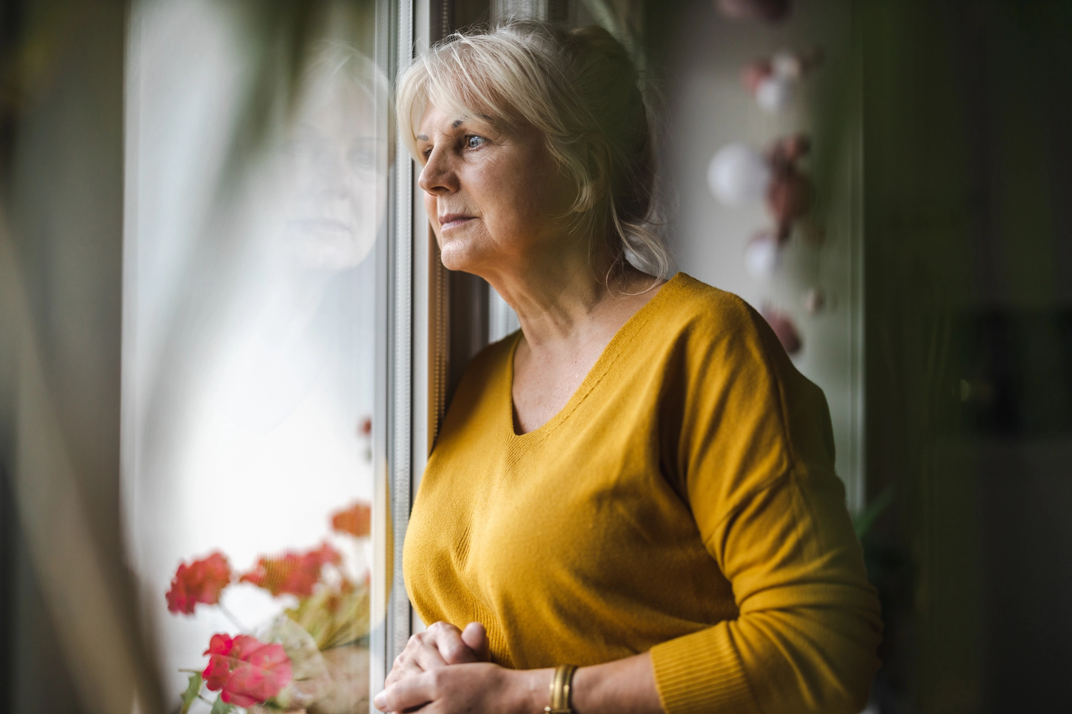 A woman looking out of a window in a yellow jumper visiblity anxious at anti social behaviour