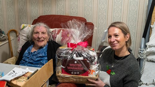 A member of RHP's community engagement team smiling and holding a hamper with a RHP customer