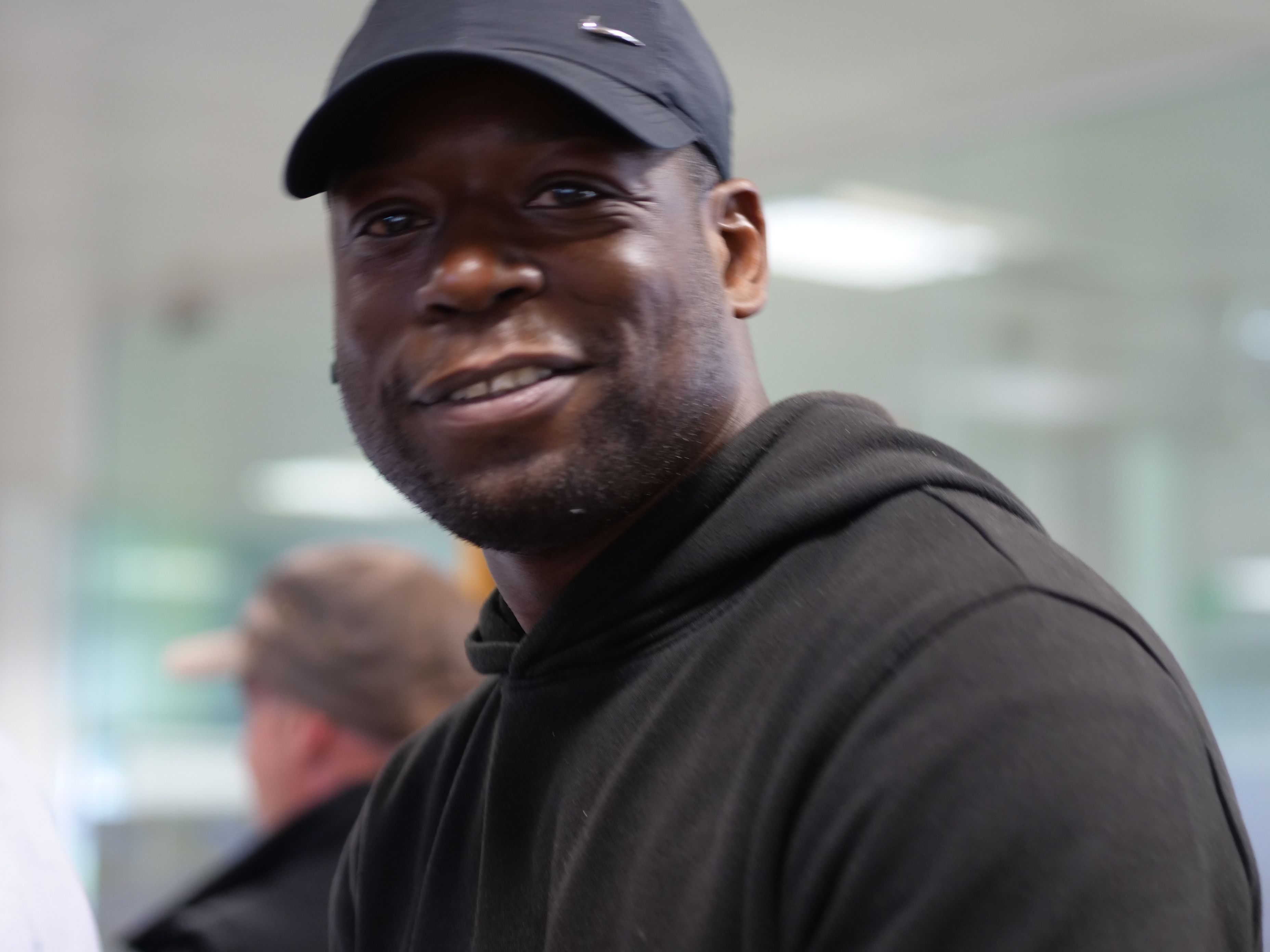 A person wearing a black cap and hoodie smiles slightly at the camera.