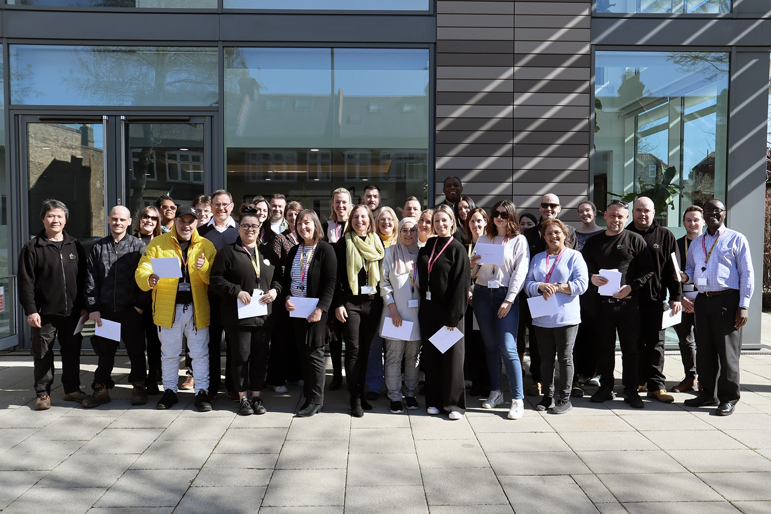 A diverse group of people stand in front of a modern glass building, smiling for the camera.