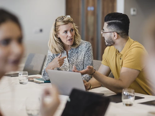 A woman and a man in discussion around a laptop in a board meeting setting