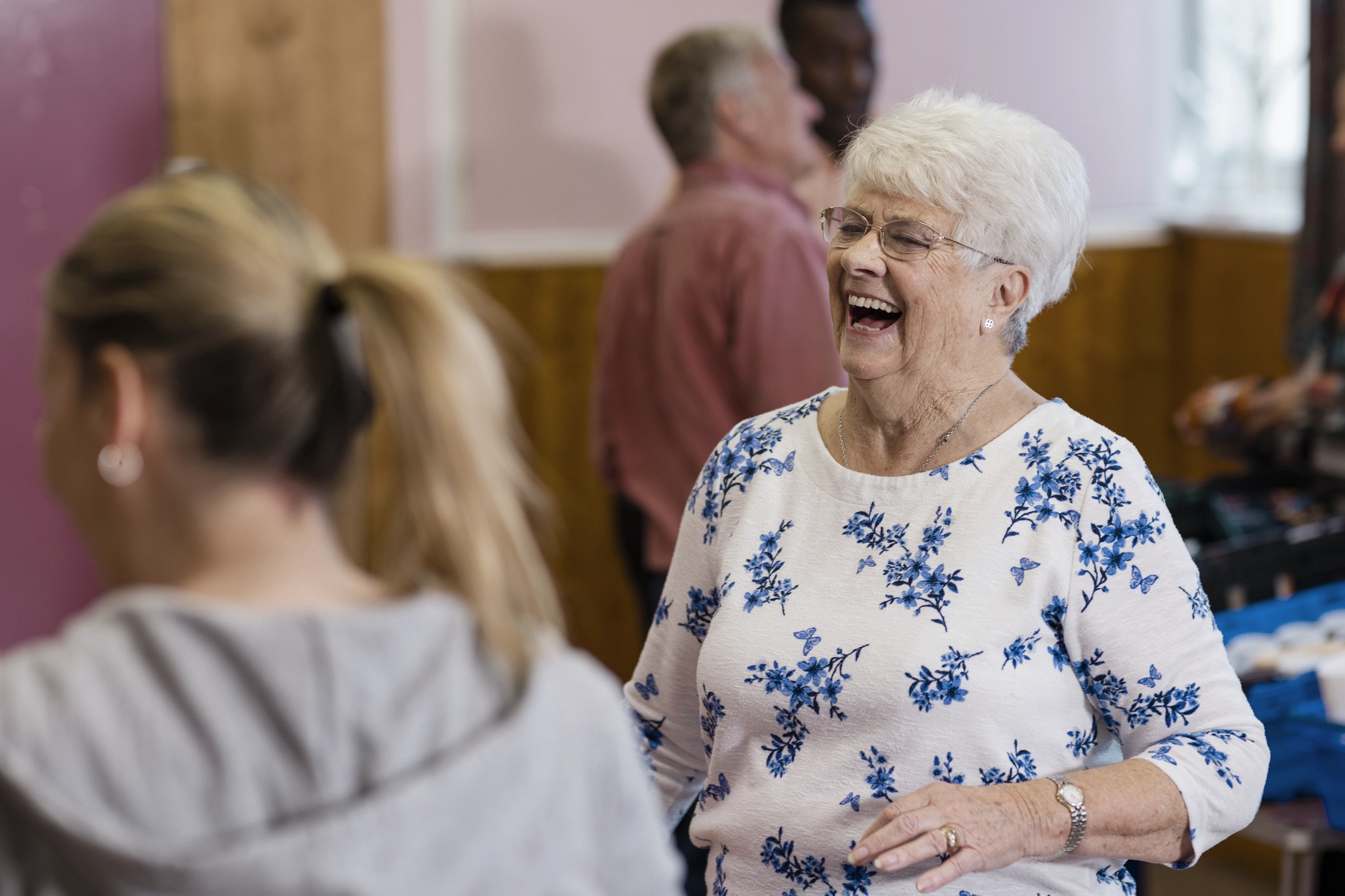 An older lady in a jumper laughing amongst some other people at a community event