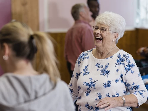 An older lady in a jumper laughing amongst some other people at a community event