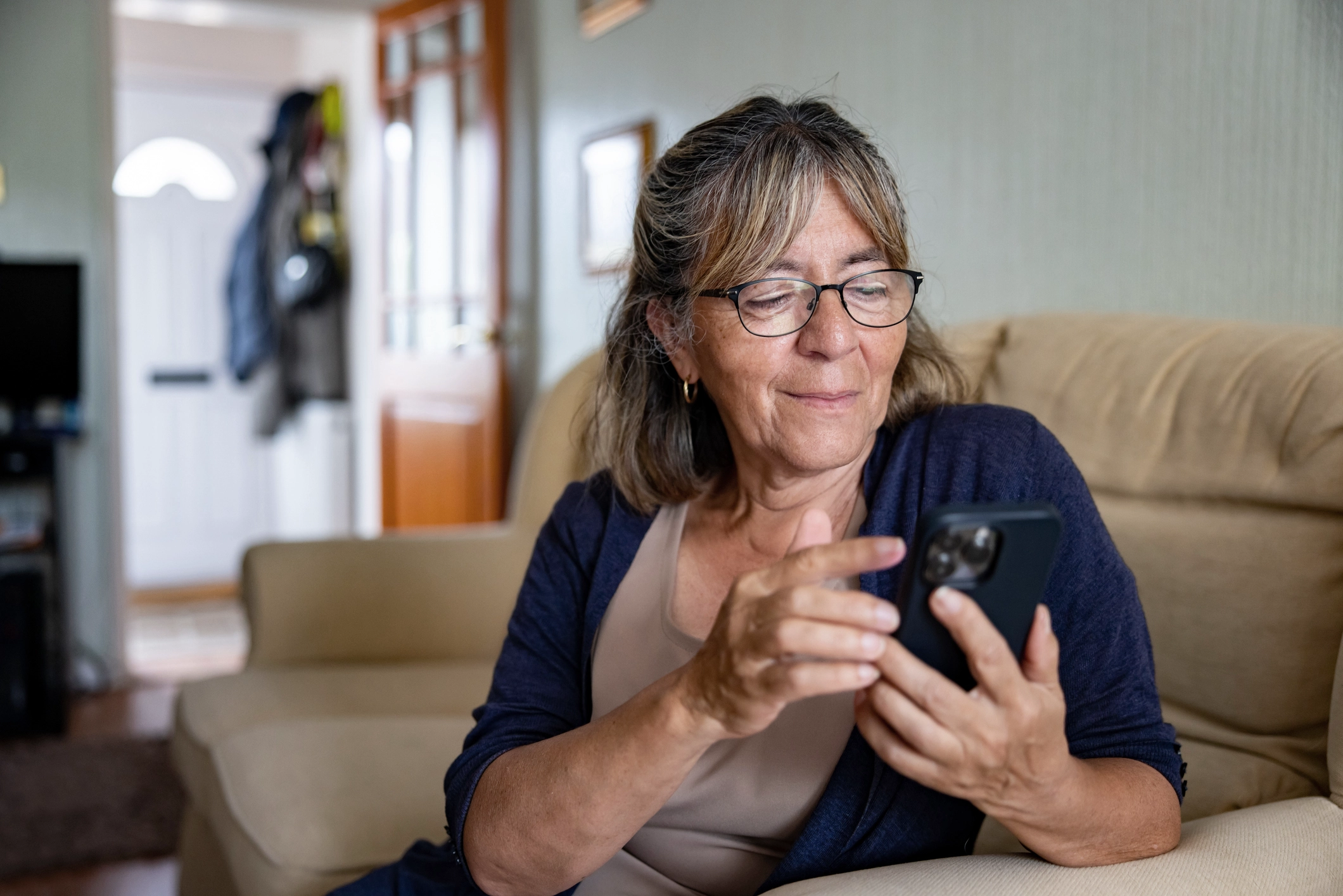 Woman At Home On A Cream Sofa Using Her Smart Phone