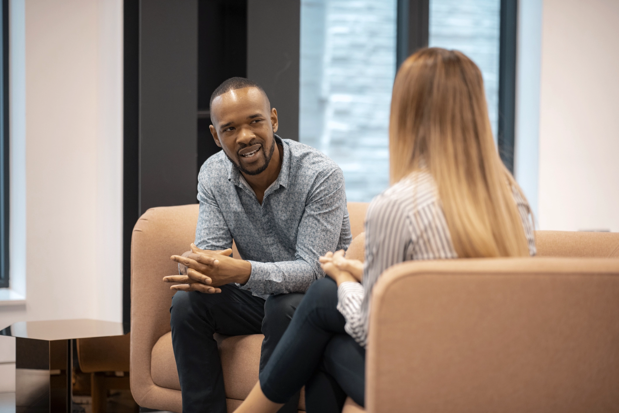 A Man Sitting In A Office Leaning Forward Talking To A Woman With A Concerned Look On His Face