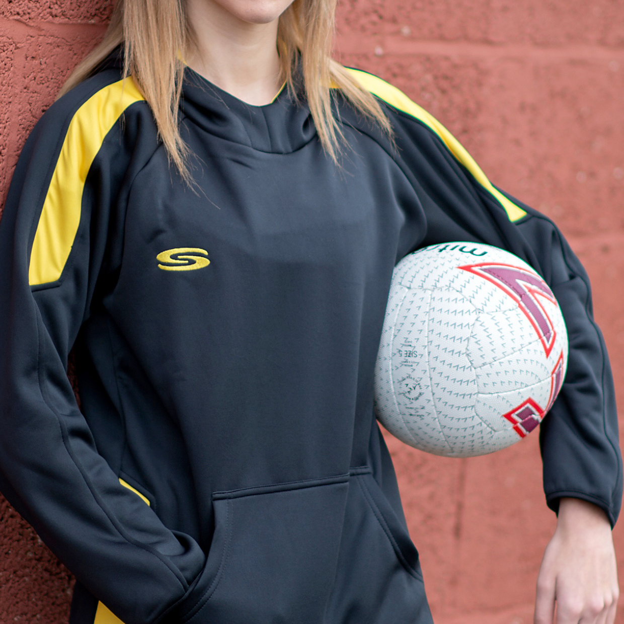 Black/yellow hoodie with a netball under the arm 
