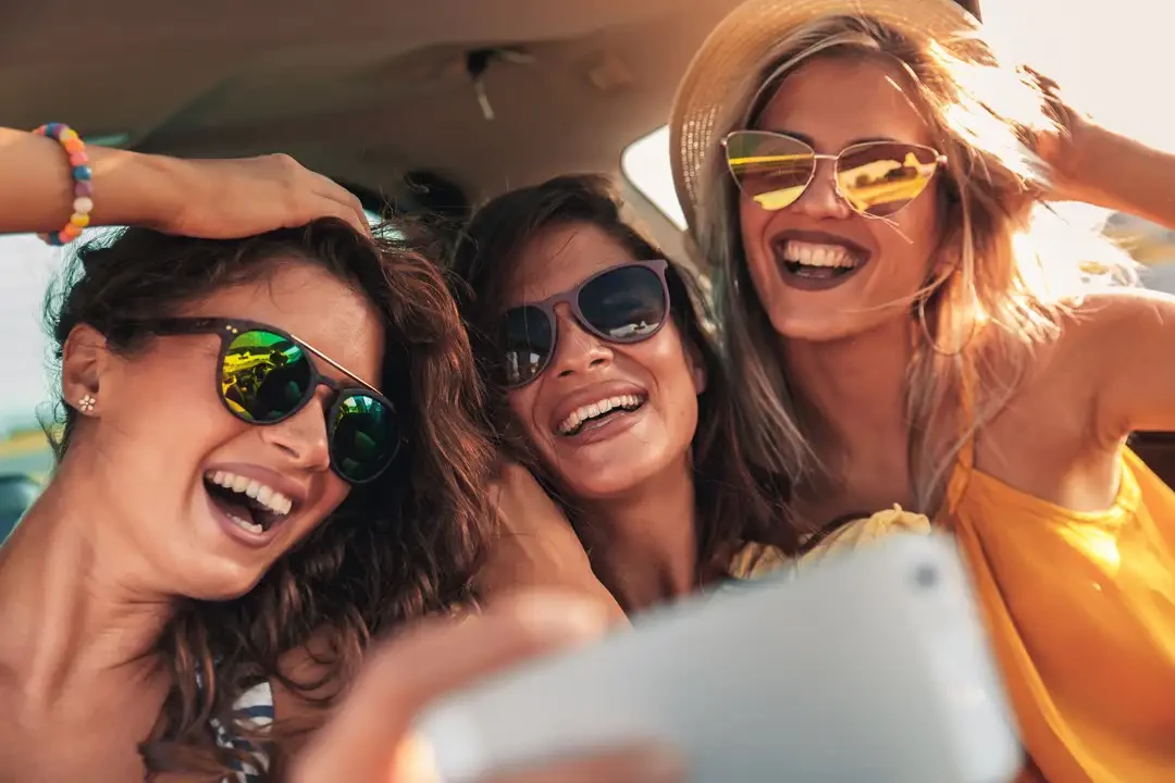 3 happy young women taking a selfie in a car